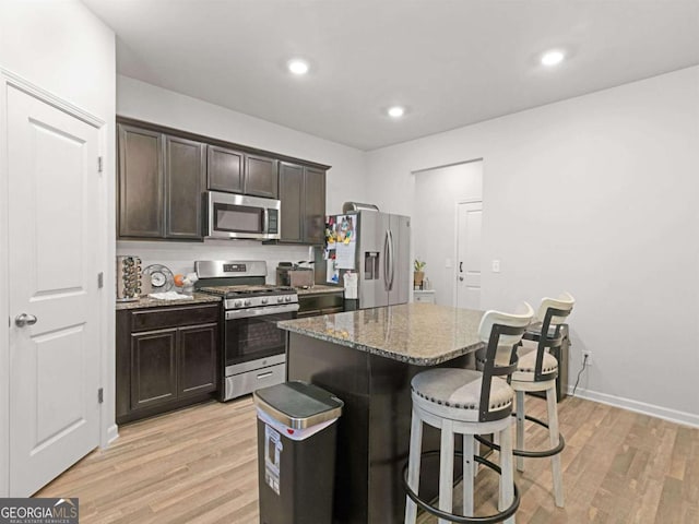 kitchen with stone countertops, a center island, stainless steel appliances, light wood-style floors, and a breakfast bar area