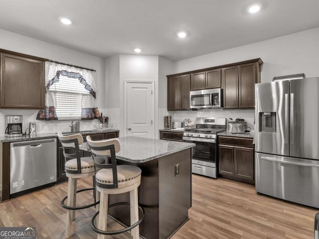 kitchen with a center island, stainless steel appliances, light wood-style floors, light stone countertops, and dark brown cabinets