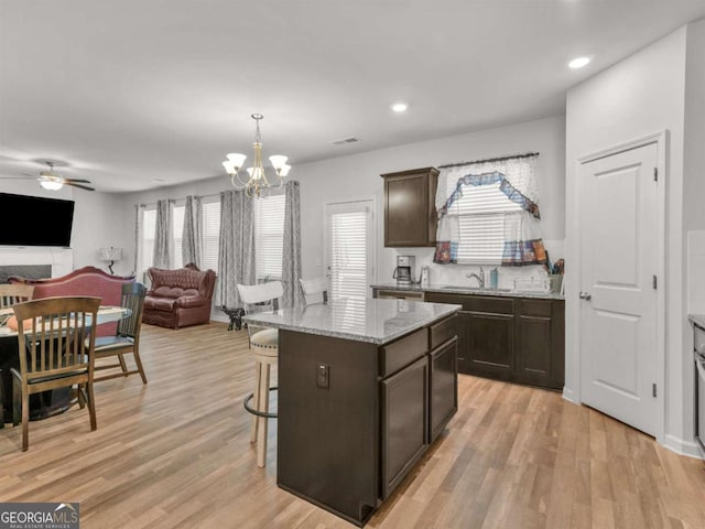 kitchen featuring light wood finished floors, light stone countertops, dark brown cabinetry, open floor plan, and a kitchen bar