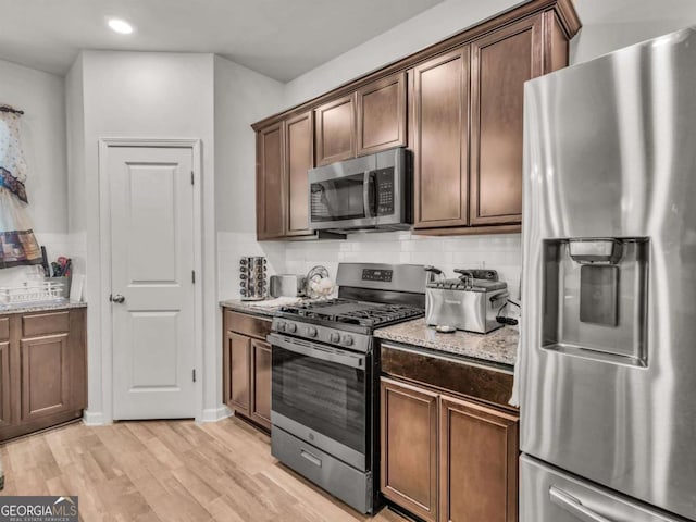 kitchen featuring recessed lighting, light wood-style floors, appliances with stainless steel finishes, decorative backsplash, and light stone countertops