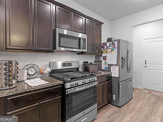 kitchen featuring stainless steel appliances, dark stone counters, light wood-style floors, decorative backsplash, and dark brown cabinets