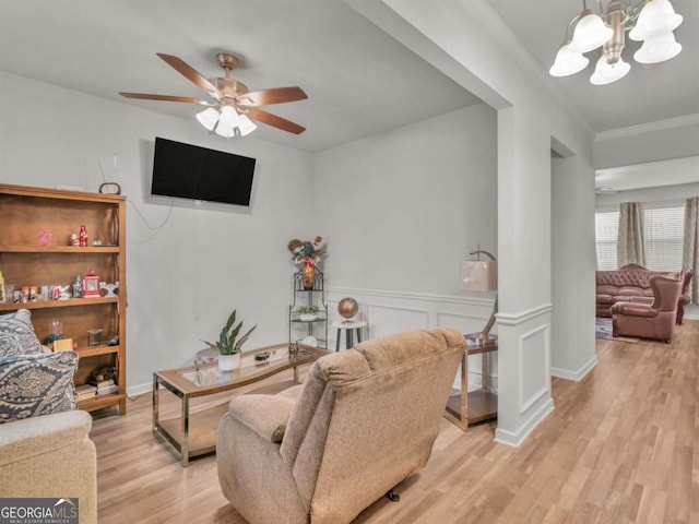 living room with ceiling fan with notable chandelier, crown molding, wood finished floors, and wainscoting