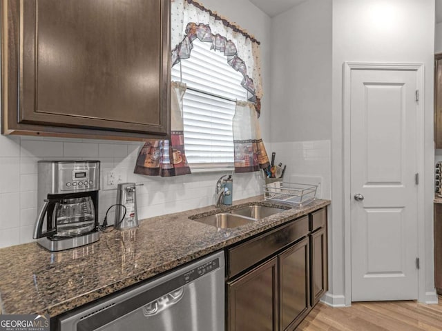 kitchen featuring light wood finished floors, dark brown cabinets, dishwasher, dark stone counters, and a sink