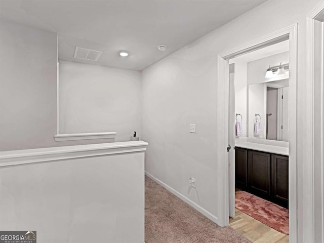 hallway with baseboards, visible vents, and light carpet