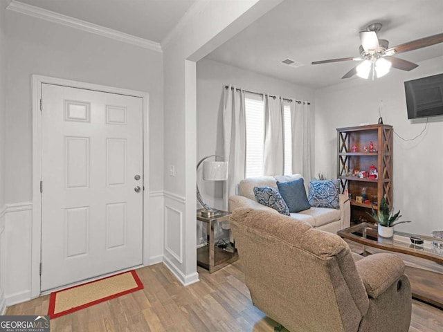 living area featuring visible vents, a wainscoted wall, ornamental molding, light wood-style floors, and a ceiling fan