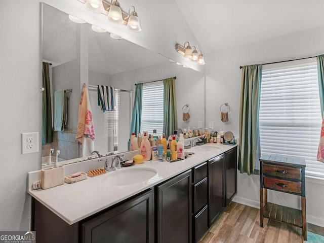 bathroom featuring lofted ceiling, wood finished floors, double vanity, and a sink