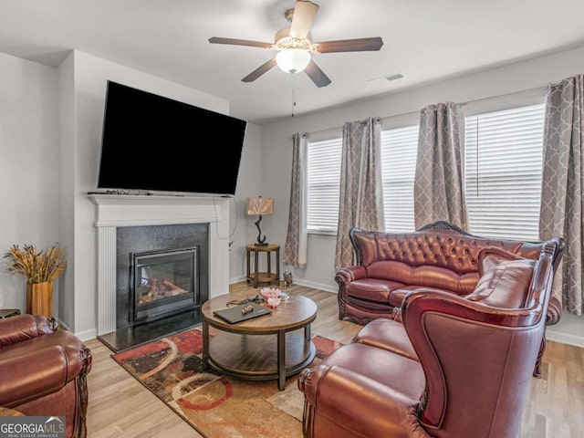 living area featuring ceiling fan, baseboards, wood finished floors, and a glass covered fireplace