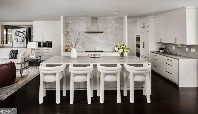 kitchen with a breakfast bar, tasteful backsplash, white cabinetry, wall chimney range hood, and dark wood-style flooring