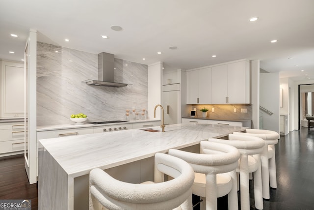 kitchen with paneled refrigerator, a sink, decorative backsplash, white cabinetry, and wall chimney range hood