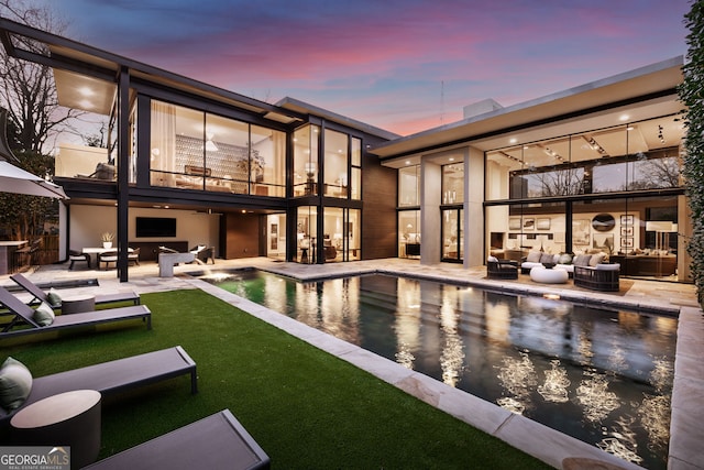 pool at dusk featuring an outdoor pool, a lawn, outdoor lounge area, and a patio area