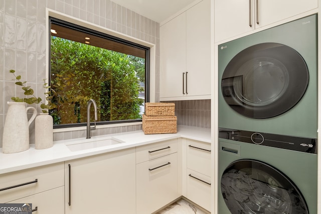 washroom with cabinet space, marble finish floor, stacked washer / drying machine, and a sink