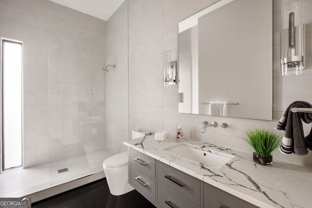 bathroom with vanity, tiled shower, tile walls, toilet, and tasteful backsplash