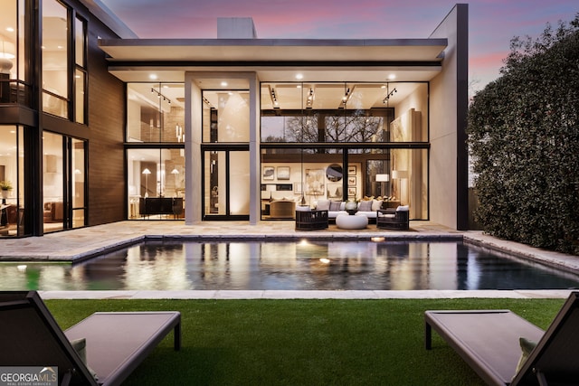 back of property at dusk featuring a patio area, an outdoor pool, outdoor lounge area, and a yard