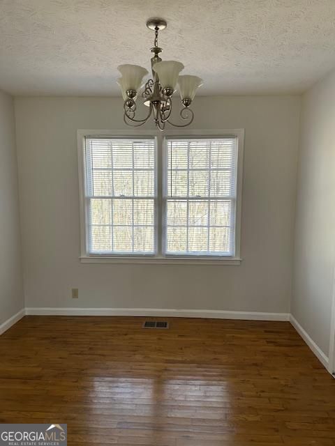 unfurnished dining area featuring wood finished floors, visible vents, a wealth of natural light, and a chandelier