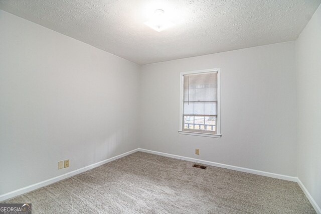 unfurnished room with a textured ceiling, carpet, visible vents, and baseboards