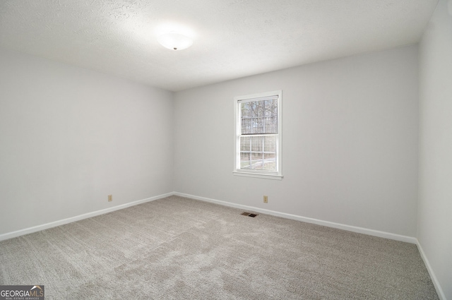 unfurnished room with visible vents, a textured ceiling, baseboards, and carpet