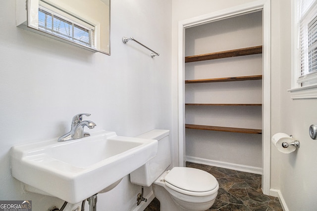 half bath with a sink, baseboards, toilet, and stone finish floor