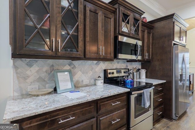 kitchen with dark brown cabinets, crown molding, light stone counters, decorative backsplash, and appliances with stainless steel finishes