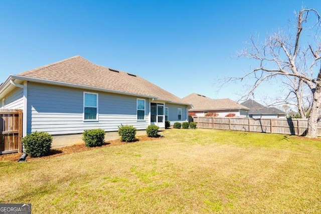 back of house featuring a lawn, roof with shingles, and fence