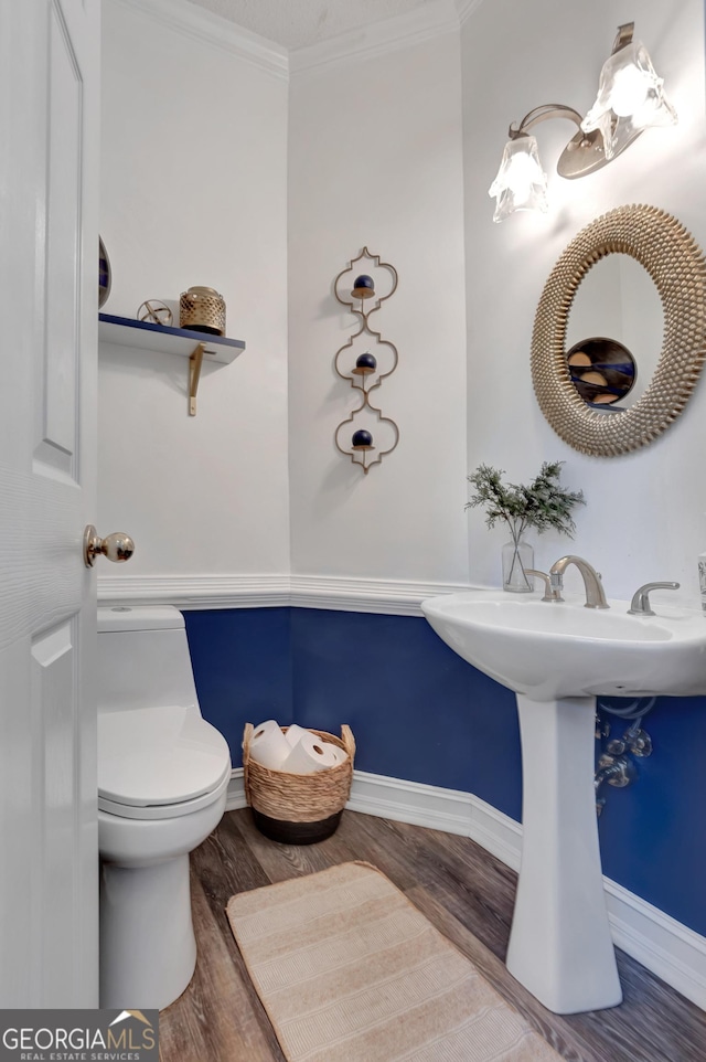 half bathroom featuring crown molding, toilet, wood finished floors, and baseboards