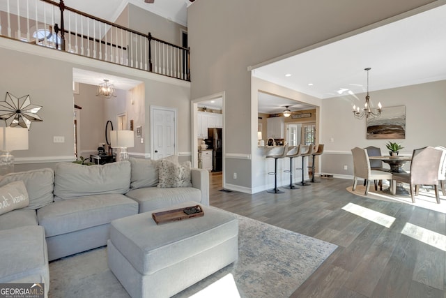 living area featuring baseboards, ornamental molding, ceiling fan with notable chandelier, a towering ceiling, and wood finished floors