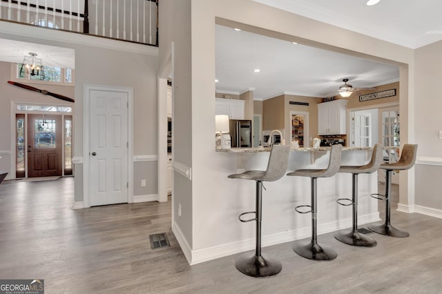 kitchen featuring visible vents, white cabinets, a breakfast bar, and crown molding