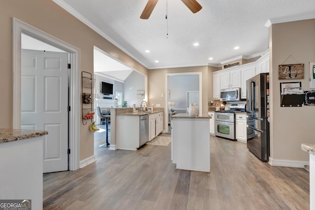 kitchen featuring ornamental molding, a sink, appliances with stainless steel finishes, white cabinetry, and light wood-type flooring