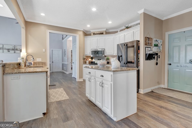 kitchen with light stone counters, wood finished floors, a sink, stainless steel appliances, and white cabinets