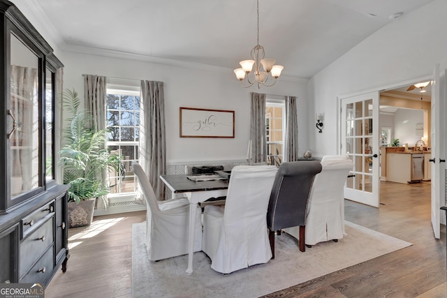 dining area with crown molding, vaulted ceiling, light wood-style flooring, french doors, and a notable chandelier