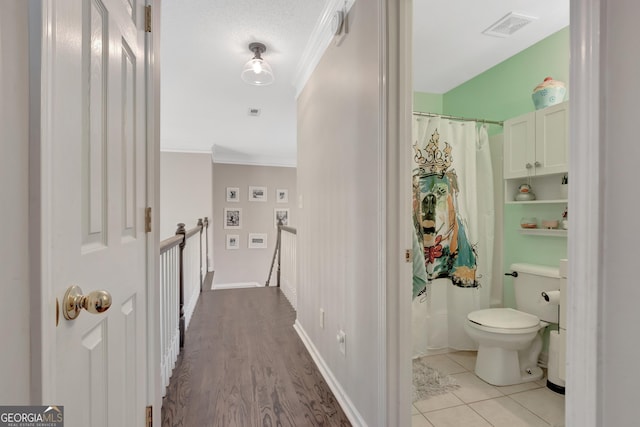 hall featuring baseboards, visible vents, ornamental molding, tile patterned floors, and an upstairs landing