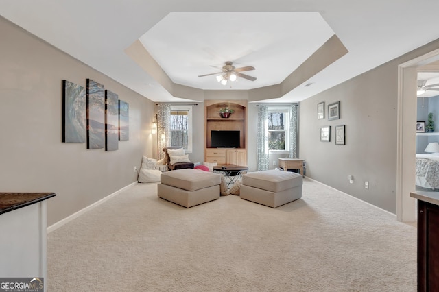 living area with baseboards, a ceiling fan, a tray ceiling, and carpet floors