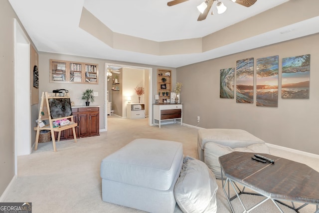 living room featuring light carpet, baseboards, a raised ceiling, and ceiling fan