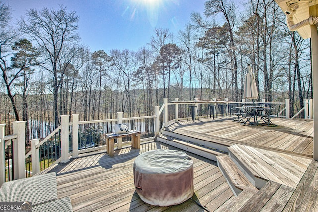 wooden terrace with outdoor dining area and a view of trees