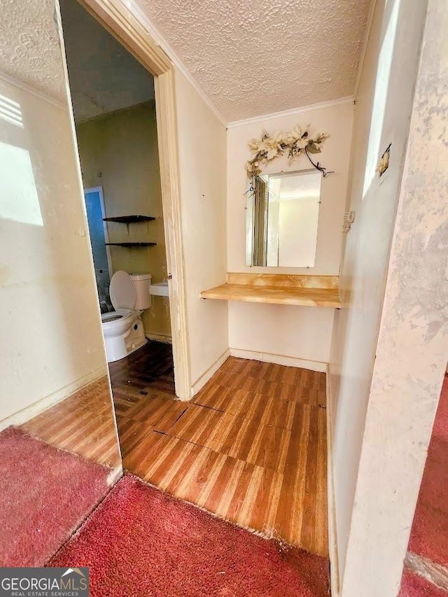 hall with ornamental molding, wood finished floors, and a textured ceiling