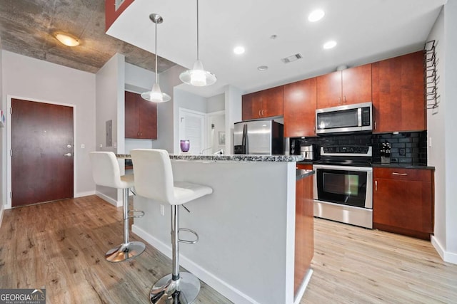 kitchen with visible vents, a kitchen breakfast bar, backsplash, appliances with stainless steel finishes, and light wood finished floors