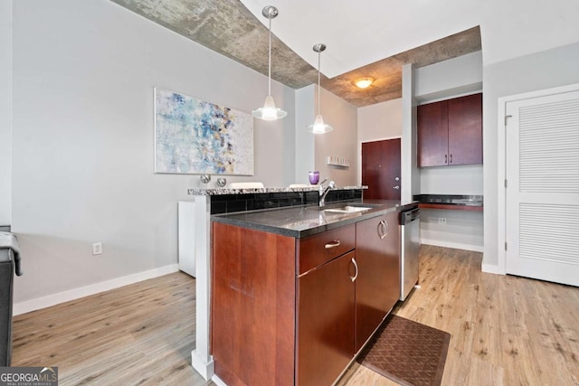 kitchen featuring light wood-type flooring, a sink, dark countertops, stainless steel dishwasher, and hanging light fixtures