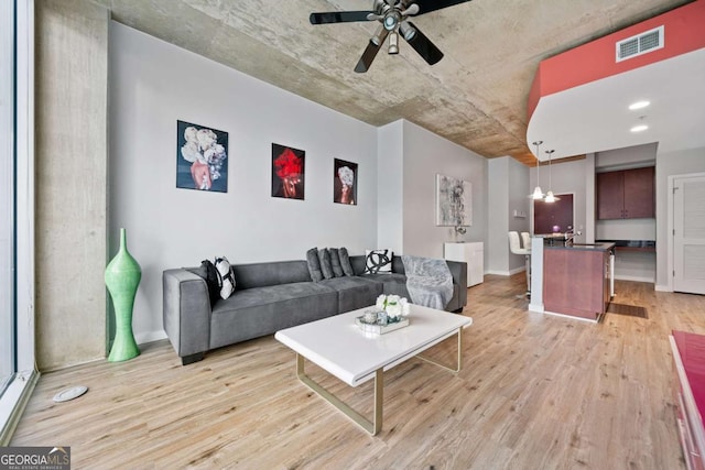 living room with light wood-type flooring, visible vents, baseboards, and ceiling fan