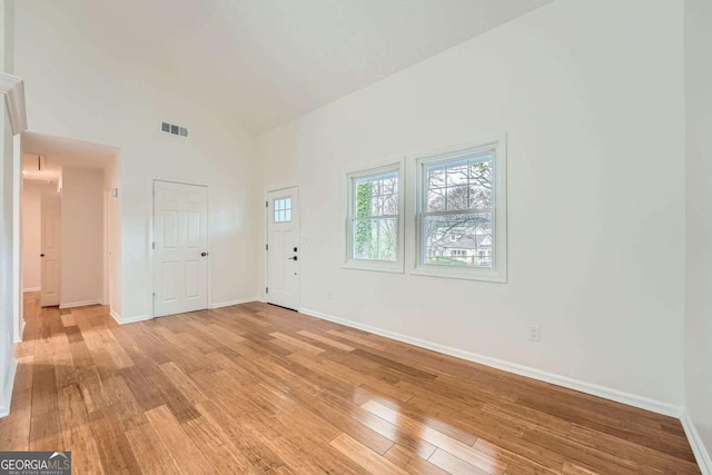 interior space with light wood finished floors, visible vents, a high ceiling, and baseboards