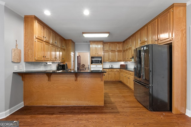 kitchen with dark countertops, a peninsula, a kitchen bar, stainless steel microwave, and black fridge