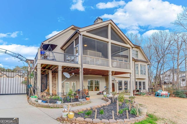 rear view of house with a gate, a sunroom, a chimney, french doors, and a patio area