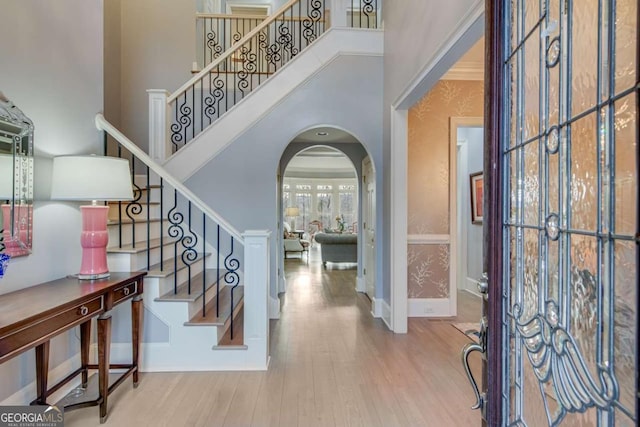 entrance foyer featuring baseboards, stairway, a towering ceiling, wood finished floors, and arched walkways