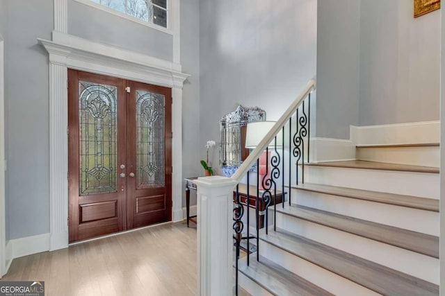 foyer entrance with french doors, baseboards, wood finished floors, and stairs