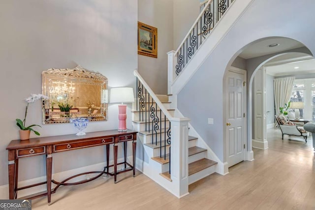 staircase featuring baseboards, arched walkways, a high ceiling, and wood finished floors