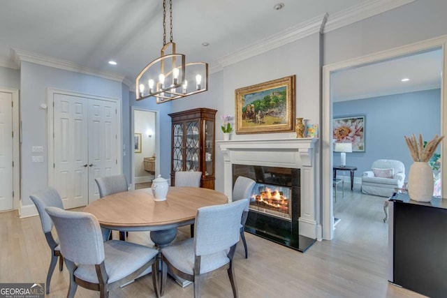 dining space with a glass covered fireplace, recessed lighting, light wood-style floors, crown molding, and baseboards