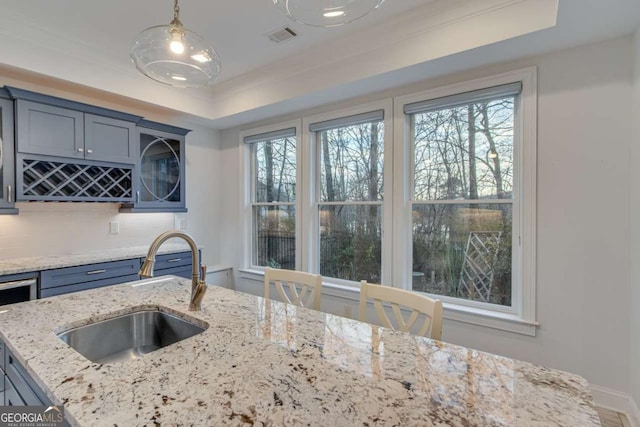 kitchen featuring visible vents, a tray ceiling, a sink, decorative backsplash, and pendant lighting