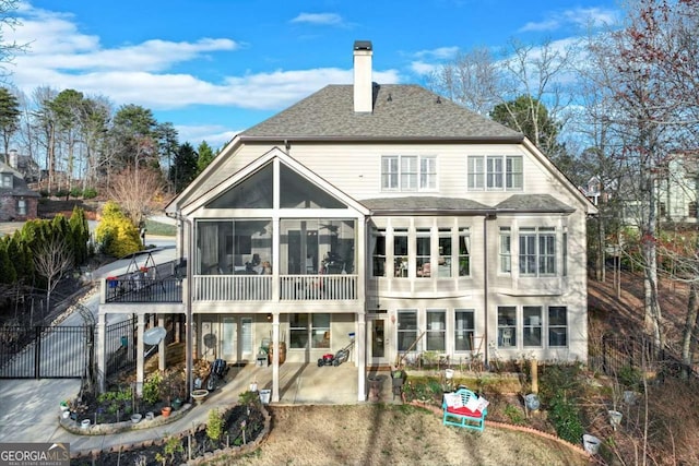 rear view of house featuring fence, roof with shingles, a chimney, a sunroom, and a patio