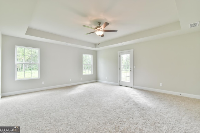 spare room featuring visible vents, baseboards, ceiling fan, light colored carpet, and a tray ceiling