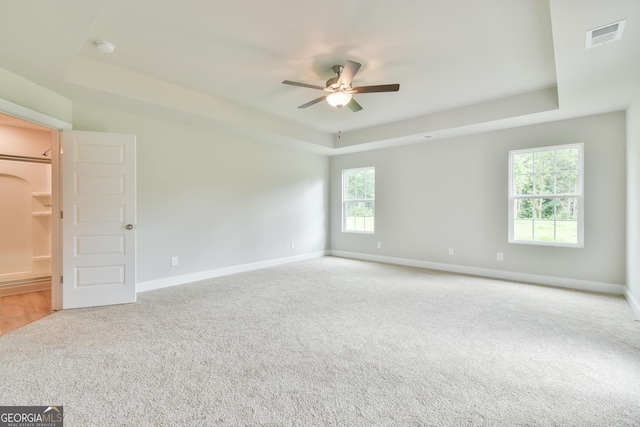 carpeted spare room with a tray ceiling, arched walkways, baseboards, and ceiling fan