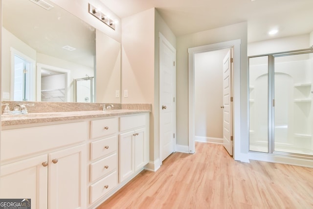 full bath with wood finished floors, double vanity, a stall shower, a sink, and a closet