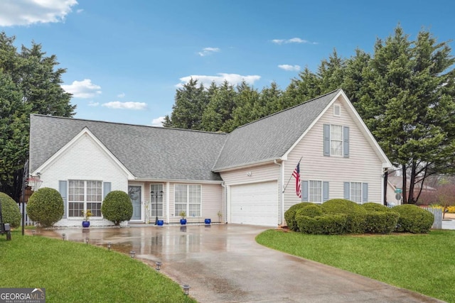 view of front of house with an attached garage, concrete driveway, a front lawn, and a shingled roof